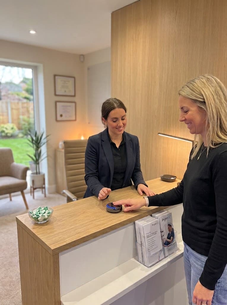 A patient using the Prysm iO device at a clinic reception desk while a receptionist assists